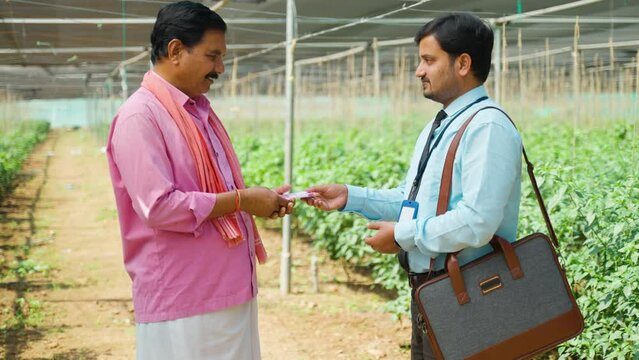 Happy farmer receiving money from banker at greenhouse as loan - concept of investment, financial support and banking assistance