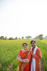 Indian farmer standing with wife at agriculture field.