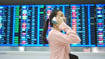 People travel on holiday vacation and airplane transportation concept. Young Asian woman holding passport and using mobile phone while checking timetable flight boarding schedule in airport terminal.