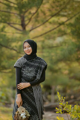young beautiful woman in hijab wearing indonesian regional ethnic dress and holding a bouquet of flowers against a nature background