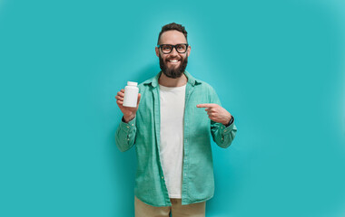 Smiling man holding a jar of medicine pills, daily vitamins and supplements. Health