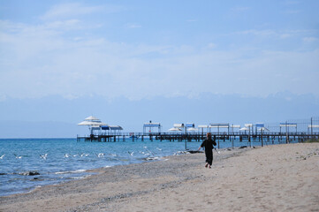 Tourism concept. Girl running and playing with seagull birds, running and jumping on a beautiful beach on a sunny day. Teenager girl running to the birds on the beach. Kyrgyzstan. Issyk-kul Lake. 