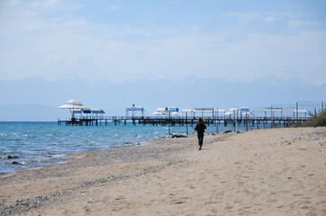 Girl running and playing with seagull birds, running and jumping on a beautiful beach on a sunny day. Teenager girl running to the birds on the beach. Kyrgyzstan. Issyk-kul Lake. Tourism concept.
