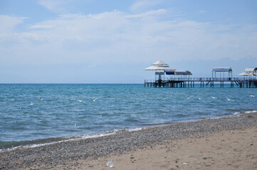 Obraz premium Summer bacground. Pier and seagulls on a sunny day. Landscape of a beautiful mountain lake. Tourism or vacation concept. Kyrgyzstan. Issyk-Kul. Color nature photo. Hello Summer.
