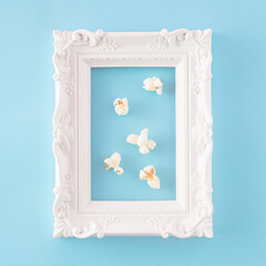 Creative aesthetic arrangement made of popcorn in a retro white frame on a blue background. Minimal gallery or movie and entertainment concept.