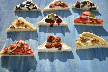 nine different toasts with various fruits, berries and nuts on blue background, top view