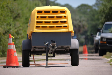 Yellow jackhammer machine with compressor trailer on road construction site