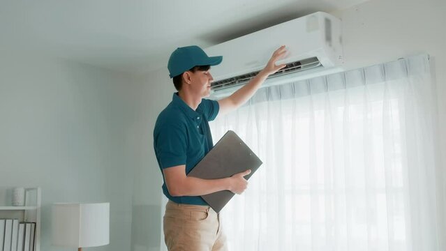 An Asian young Technician service man wearing blue uniform checking ,  cleaning air conditioner in home