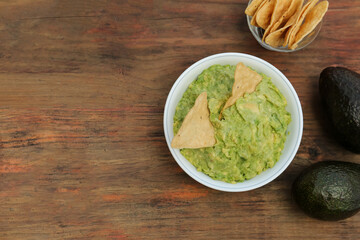 Delicious guacamole, avocados and nachos on wooden table, flat lay. Space for text