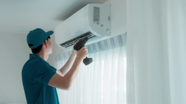 An Asian young Technician service man wearing blue uniform checking ,  cleaning air conditioner in home