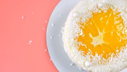 Cake with orange and coconut shavings spun on a pink background.