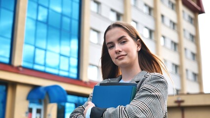 A young girl student walks through the city with folders in her hands.