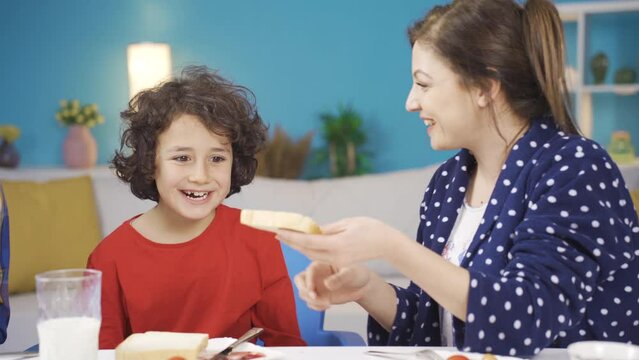 Happy family morning breakfast. The child is looking hungrily at the table.
Happy family is having breakfast together at the weekend, mother spreads jam on her bread and feeds her son.
