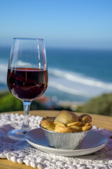 Pairing of Portugeese food and drink, glass of tawny porto wine and chicken pie empada de frango, served outdoor with view on blue Atlantic ocean near Sintra in Lisbon area, Portugal