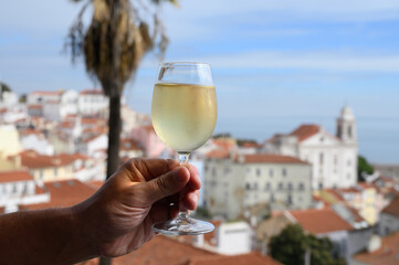 Hand with glass of cold white Portuguese wine in outdoor cafe at view point on old part of Lisbon city, Portugal
