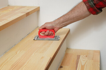 Closeup of worker hand sanding wooden stairs using  hand tool