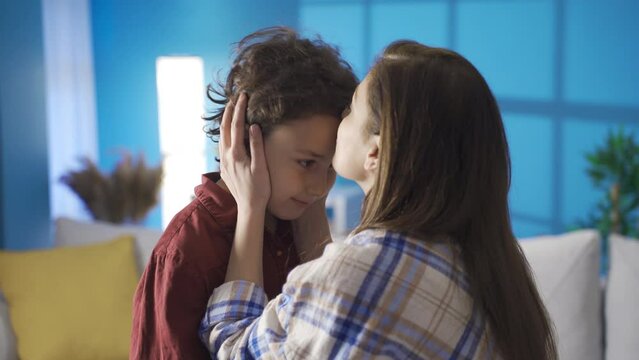 Emotional mother kissing her son at home and looking at him proudly.
The mother raises her son with compassion and love, kisses him on the forehead and is proud of him.
