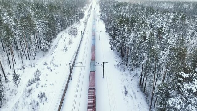 Freight train rides in the middle of a winter snowy forest. Aerial view
