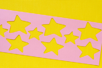 pink paper stencil with star cutouts on yellow corrugated paper texture