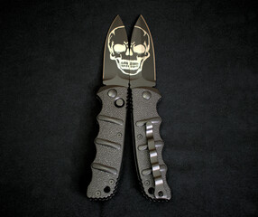 Folding knives cutting skull etching black stainless steel blade and handle textile background