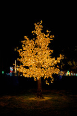 plastic tree with yellow light bulbs in the middle of the park. christmas decoration at Alcala park in Bogota in Colombia. christmas lights on tree. plastic tree leaves glowing 