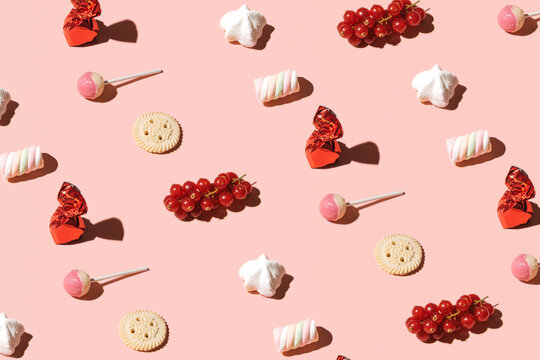 Cookies, lollypops, bonbons and berry fruit, creative candy pattern against pastel pink background. Summer aesthetic idea. 