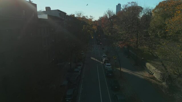Street between city park and row of classic apartment houses in urban borough. Forwards fly place in shadow. New York City, USA