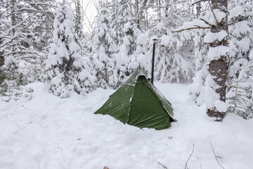 A green hot tent stands in a snowy forest while winter camping in Algonquin Provincial Park 