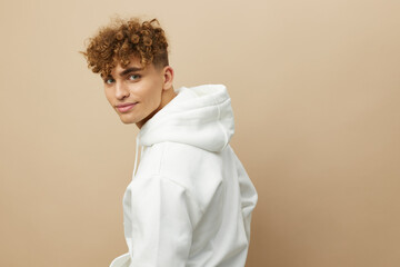 a happy, attractive man stands on a beige background in a light hoodie with his back to the camera, and turning his head back smiling pleasantly