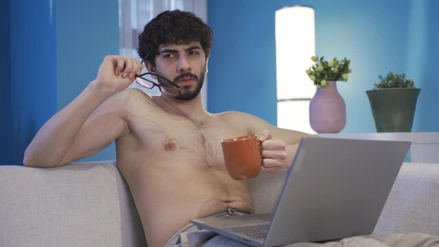 Handsome young man with curly hair using laptop is thoughtful and naked.
Attractive Young Man Thinking, Working From Home, Shopping Online, Watching Videos or Writing Emails.
