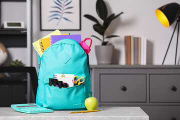 Turquoise backpack and different school stationery on table indoors, space for text