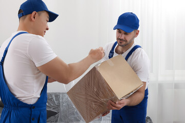 Workers wrapping box in stretch film indoors
