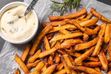 Delicious sweet potato fries and sauce on parchment paper, closeup