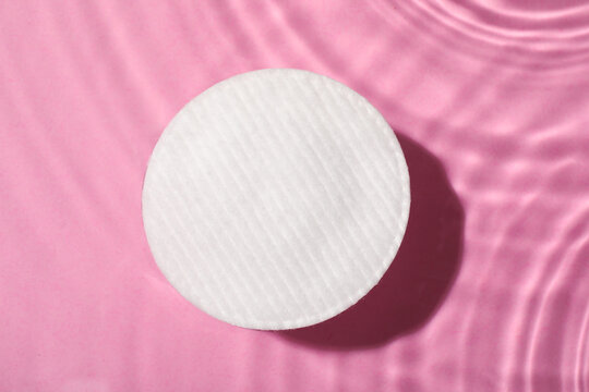 Cotton pad and micellar water on pink background, top view