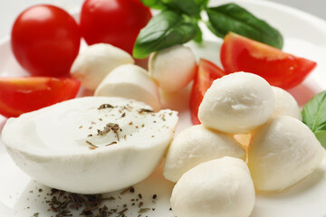 Delicious mozzarella with tomatoes and basil leaves on white plate, closeup