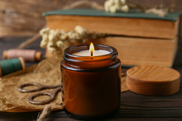 Burning scented candle, book and flowers on wooden table, closeup