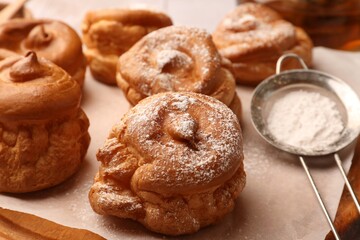 Delicious profiteroles with powdered sugar on wooden board, closeup