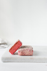 Pink lamingtons on a plate Australian raspberry lamingtons, small cakes covered in desiccated coconuts