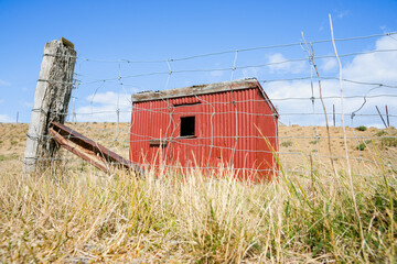 Fototapeta na wymiar Characteristic red corrugated iron shed through farm fence on Central Otago Rail Trail