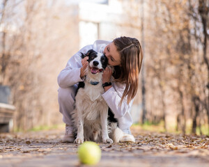 Caucasian woman hugging her dog on a walk in the autumn park. Border collie looks at the ball.