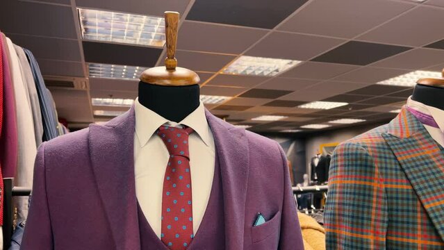 Mannequins in men's classic suits with shirts and ties stand in the window of a clothing store.