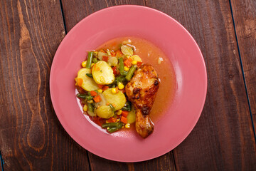 Baked chicken drumstick with vegetables potatoes green beans in sauce and spices on a wooden table.