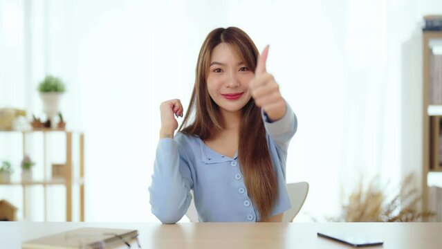 Happy teen asian girl blogger smiling face waving hand talking to webcam recording vlog, social media influencer streaming, making video call at home. She thumb up good or better