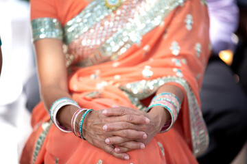 Indian wedding guests are seated hand in hand in orange sari adorned with glittering jewelry. On his hand he wears multi-colored bracelets.