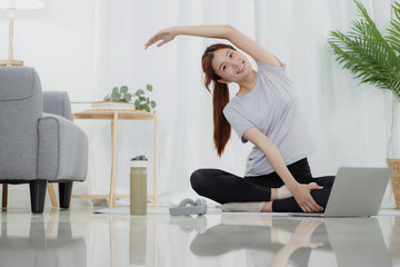 Young asian woman attractive exercises workout at home and watching Online sports tutorials over laptop