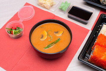 Delicious Japanese tom yum soup, rolls with salmon, avocado, cucumber, cheese in takeout packaging with wood sticks and soy sauce. Selective focus. Asian food and delivery concept. Healthy eating