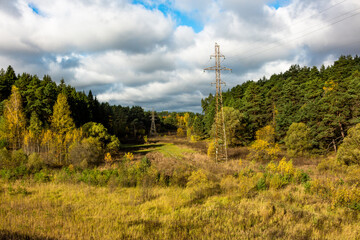 Obraz premium High-voltage power line passing through a picturesque valley surrounded by autumn nature, electric wires suspended on high metal poles
