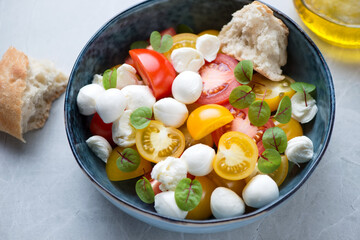 Salad with red and yellow tomatoes, mini mozzarella and beetroot leaves in a dark-blue bowl, middle closeup on a grey granite background