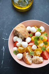 Tomato salad with mini mozzarella balls and fresh beetroot leaves, elevated view on a black marble background, vertical shot