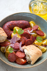Closeup of salad with yellow tomatoes, warm chorizo sausage and red onion, vertical shot, selective focus